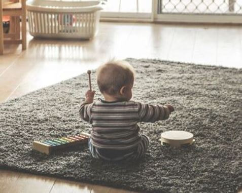 Infant sits on carpet playing xylophone at childcare of southwest Florida 